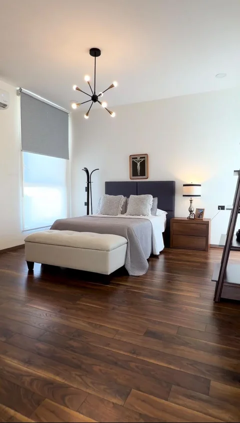 Recámara con cama, banca, ventana con persiana, minisplit y piso de madera