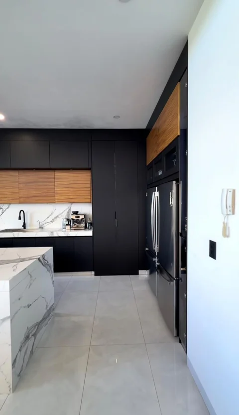 Cocina con isla, mesadas de cuarzo, alacena, refrigerador de acero y gabinetes negros y de madera