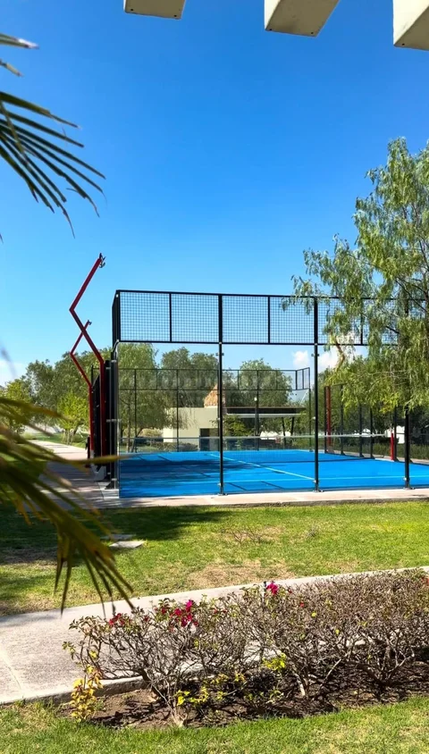 Cancha de pádel con piso azul y malla, rodeada de áreas verdes dentro del residencial