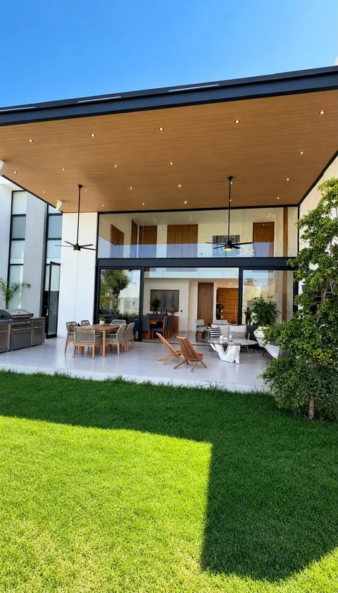 Jardín con terraza techada, comedor y asador al aire libre, y sala-comedor a doble altura al fondo